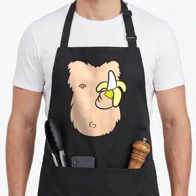 Tablier de cuisine noir avec illustration d'un singe torse nu tenant une banane jaune pelée.