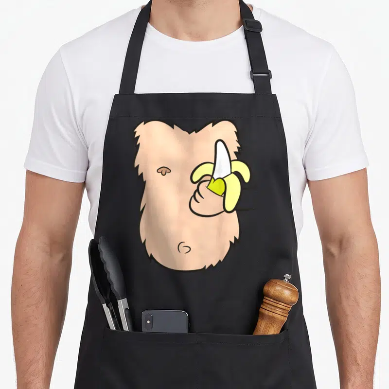 Tablier de cuisine noir avec illustration d'un singe torse nu tenant une banane jaune pelée.