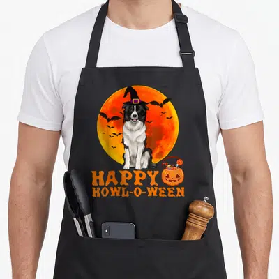 Tablier de cuisine noir avec un Border Collie en chapeau de sorcière devant une lune orange et le texte Happy Howl-O-Ween.