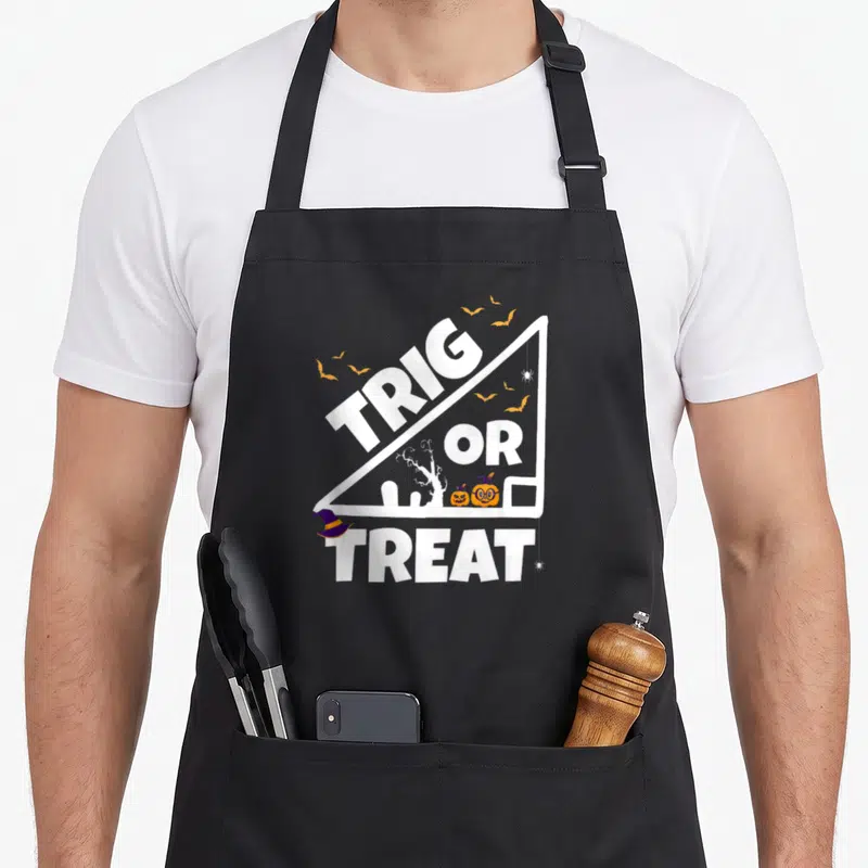 Tablier de cuisine noir avec un triangle blanc contenant le texte Trig or Treat et des citrouilles Halloween.