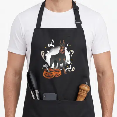 Tablier de cuisine noir avec illustration d'un Doberman entouré de fantômes et de citrouilles d'Halloween.