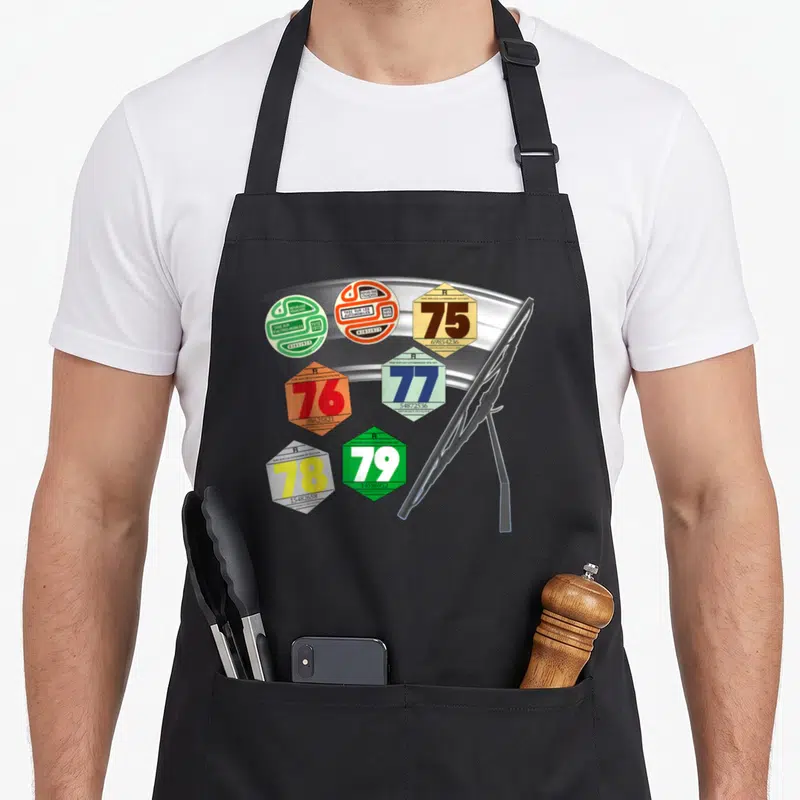 Tablier de cuisine noir avec vignettes automobiles colorées des années 70 et un balai de pare-brise illustré en gris.