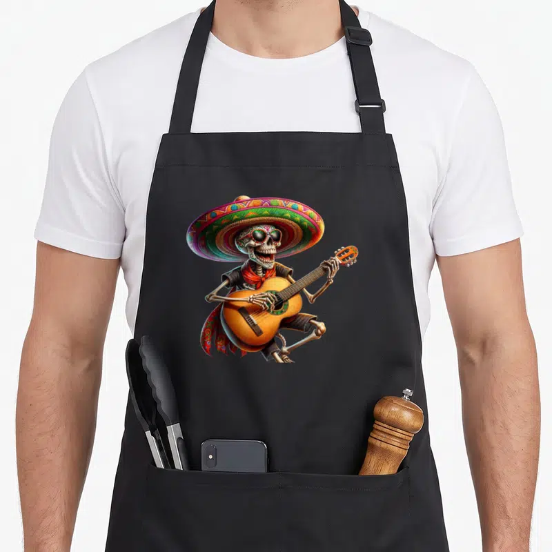 Tablier de cuisine noir avec squelette mariachi jouant de la guitare sous un grand sombrero multicolore.