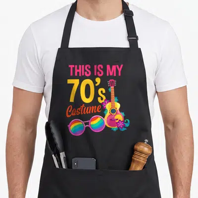 Tablier de cuisine noir avec illustration guitare, lunettes arc-en-ciel et texte This Is My 70s Costume coloré.