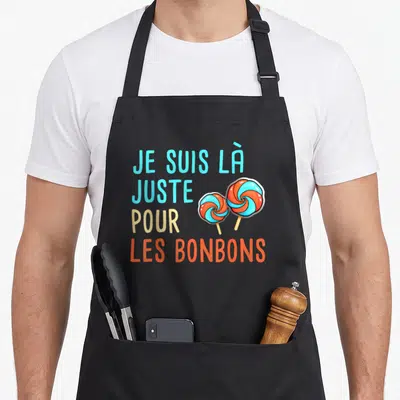 Tablier de cuisine noir avec le texte Je Suis Là Juste Pour Les Bonbons et deux sucettes orange et bleues.