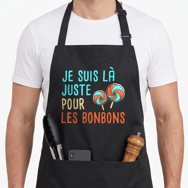 Tablier de cuisine noir avec le texte Je Suis Là Juste Pour Les Bonbons et deux sucettes orange et bleues.