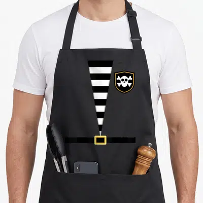 Tablier de cuisine noir avec illustration tunique pirate rayée et boucle dorée sous écu crâne et os croisés.