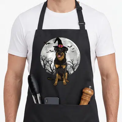 Tablier de cuisine noir avec un chien Beauceron portant un chapeau de sorcière devant une pleine lune et des chauves-souris.