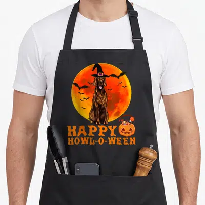 Tablier de cuisine noir avec un setter irlandais en chapeau de sorcière devant une lune orange et le texte Happy Howl-O-Ween.