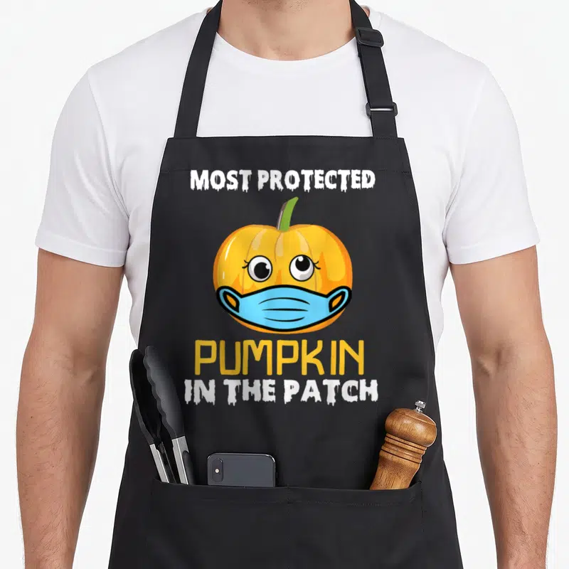 Tablier de cuisine noir avec un pumpkin portant un masque bleu et le texte Most Protected Pumpkin in the Patch.