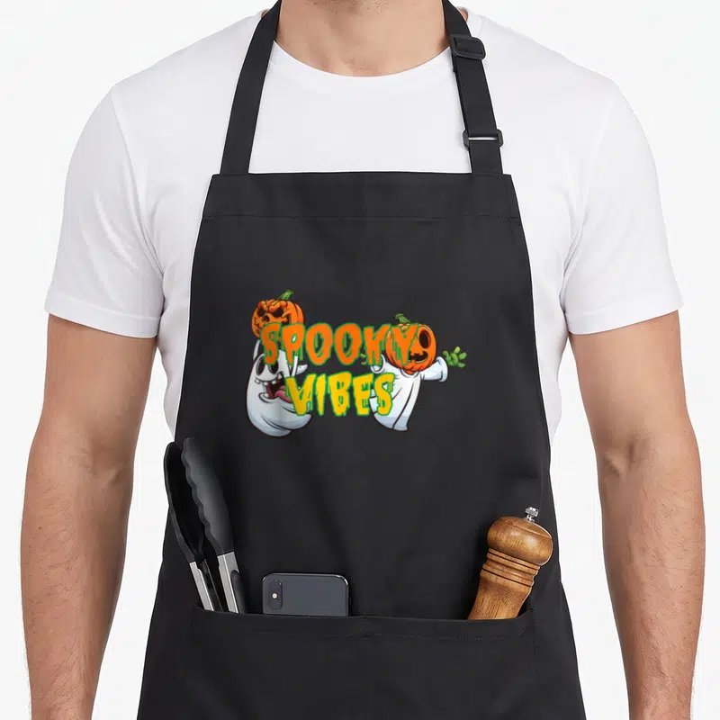 Tablier de cuisine noir avec deux fantômes en cartoon portant des citrouilles et le texte « Spooky Ambiance » au centre.