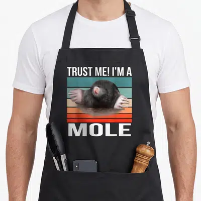 Tablier de cuisine noir avec illustration d'une taupe et texte TRUST ME I'M A MOLE sur bandes colorées.