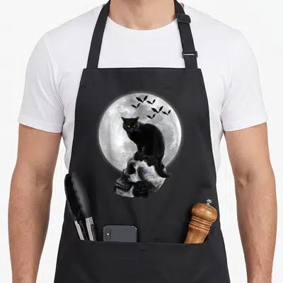 Tablier de cuisine noir avec illustration d'un chat noir sur un crâne devant une pleine lune et des chauves-souris.