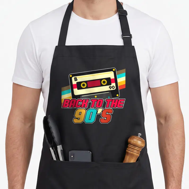 Tablier de cuisine noir avec illustration de cassette audio vintage et texte Back to the 90s multicolore.
