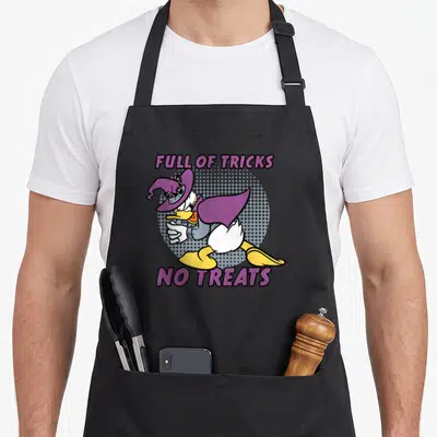 Tablier de cuisine noir avec Donald Duck en sorcier et texte Full of Tricks No Treats imprimé en violet.