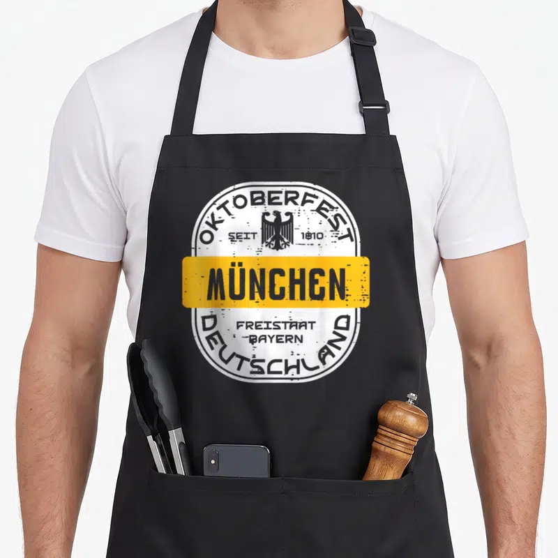 Tablier de cuisine noir avec logo Oktoberfest München Deutschland et aigle stylisé sur fond blanc vieilli.