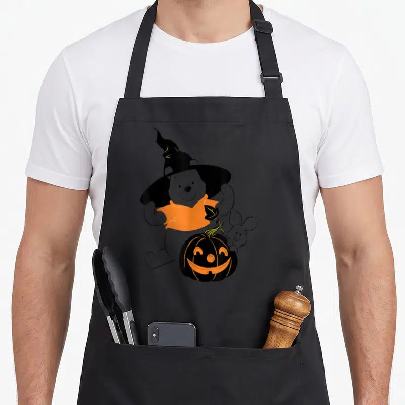 Tablier de cuisine noir avec Winnie l'Ourson en chapeau de sorcière tenant un pumpkin orange.