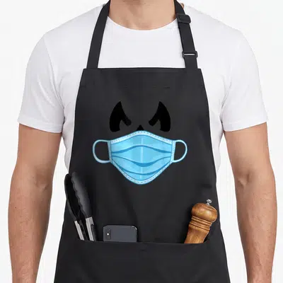 Tablier de cuisine noir avec illustration de masque chirurgical bleu et yeux noirs menaçants au-dessus.