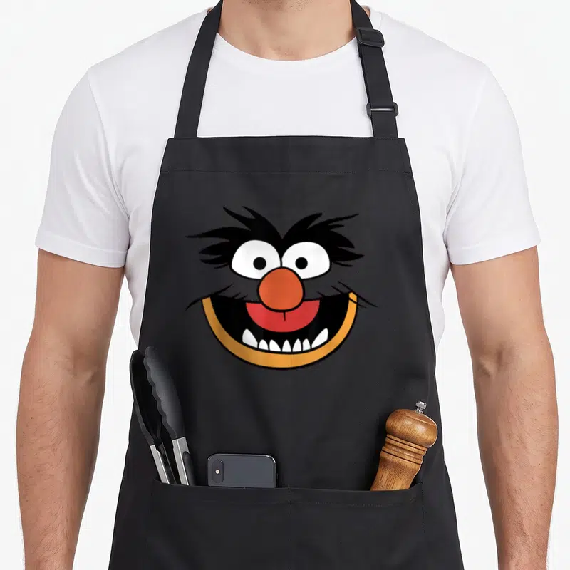 Tablier de cuisine noir avec le visage coloré et souriant du personnage Animal des Muppets en gros plan.
