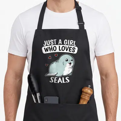 Tablier de cuisine noir avec un phoque gris souriant et le texte Just A Girl Who Loves Seals en blanc et noir.