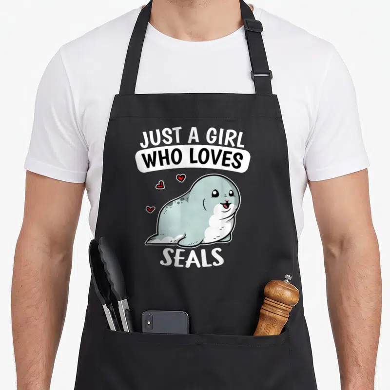 Tablier de cuisine noir avec un phoque gris souriant et le texte Just A Girl Who Loves Seals en blanc et noir.