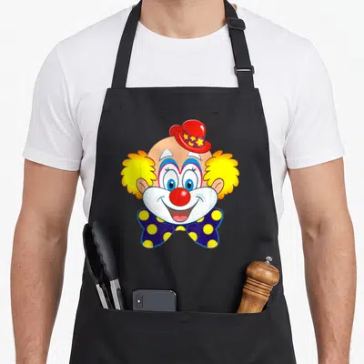 Tablier de cuisine noir avec une illustration de tête de clown souriant au chapeau rouge et nœud papillon bleu à pois jaunes.