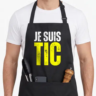 Tablier de cuisine noir avec inscription Je Suis Tic en blanc et jaune vif sur fond uni.