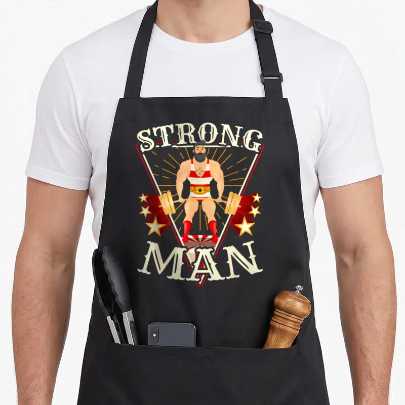 Tablier de cuisine noir avec illustration rétro d'un homme fort tenant une barre de poids encadré par le texte Strong Man.
