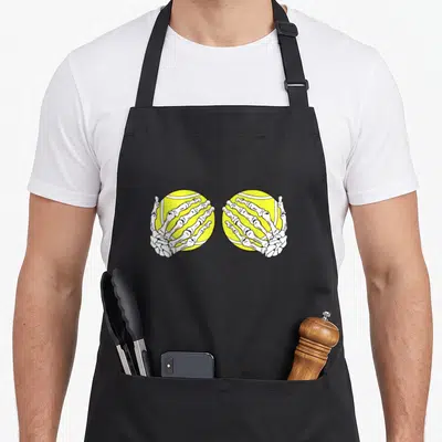 Tablier de cuisine noir avec deux mains squelettiques tenant des balles de tennis jaunes.