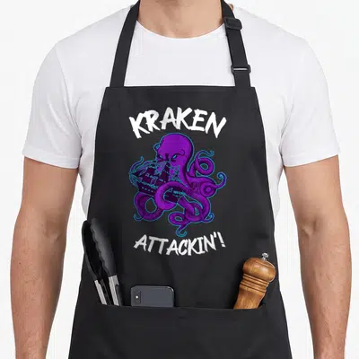 Tablier de cuisine noir avec un kraken violet attaquant un navire et le texte Attackin en blanc.
