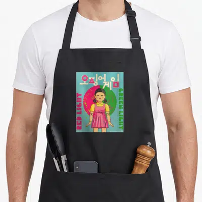 Tablier de cuisine noir avec une illustration de poupée coréenne et des textes colorés sur fond bleu.