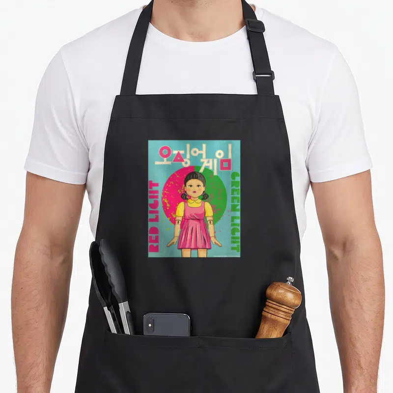 Tablier de cuisine noir avec une illustration de poupée coréenne et des textes colorés sur fond bleu.