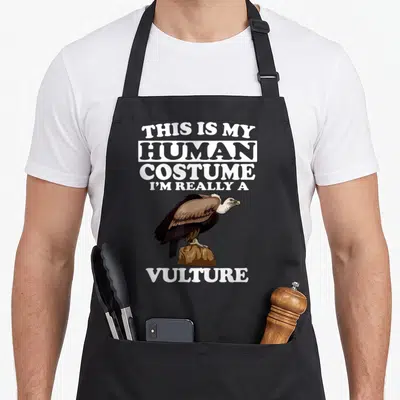 Tablier de cuisine noir avec illustration de vautour et texte blanc humoristique sur fond uni.