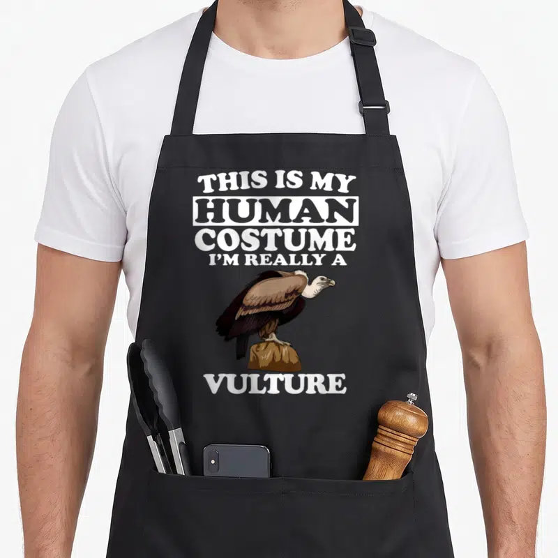 Tablier de cuisine noir avec illustration de vautour et texte blanc humoristique sur fond uni.