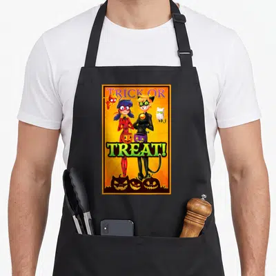 Tablier de cuisine noir avec Ladybug et Chat Noir en tenue d'Halloween tenant des paniers à bonbons.