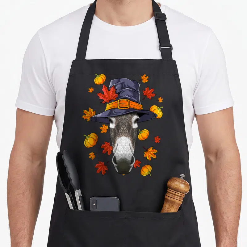 Tablier de cuisine noir avec illustration d'un animal portant un chapeau de pèlerin orné de feuilles d'érable et de pumpkins.