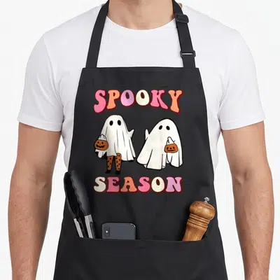 Tablier de cuisine noir avec deux fantômes blancs tenant des paniers de pumpkin et le texte Spooky Season en lettres arc-en-ciel.