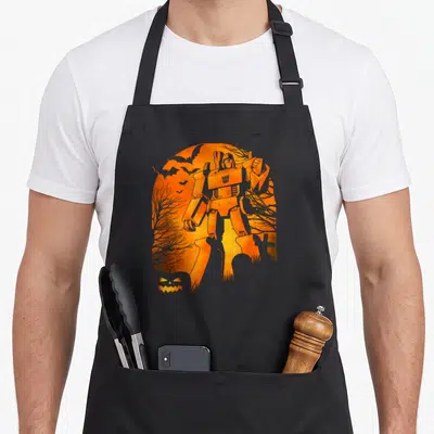 Tablier de cuisine noir avec silhouette de fantôme orange contenant Megatron Transformers et une pumpkin jack-o-lantern en bas à gauche.