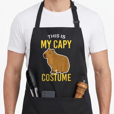 Tablier de cuisine noir avec illustration de capybara et texte This Is My Capy Costume en jaune et blanc.