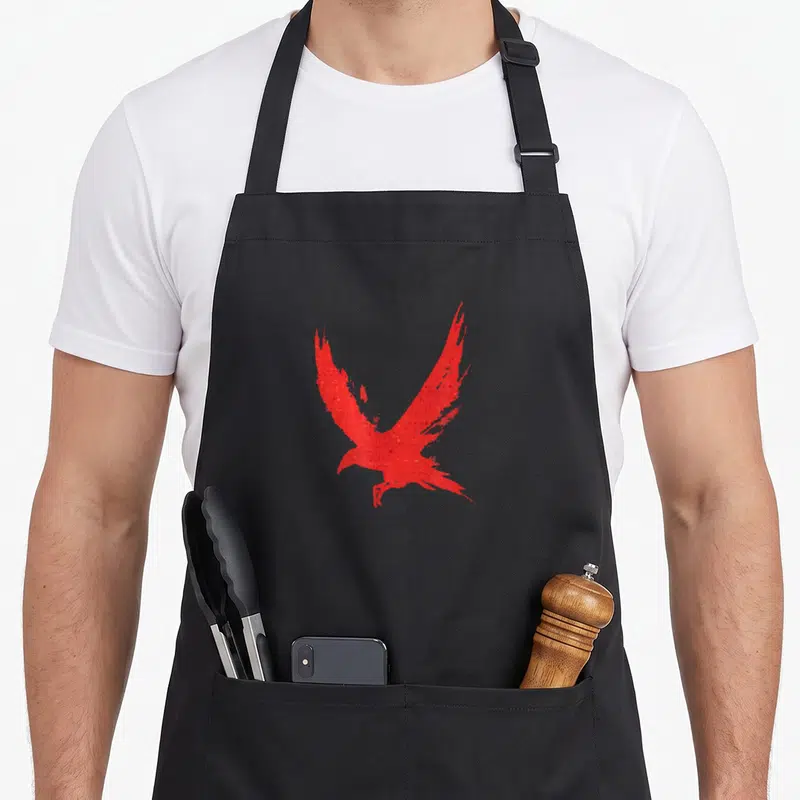 Tablier de cuisine noir avec silhouette de corbeau rouge aux ailes déployées et texture granuleuse.