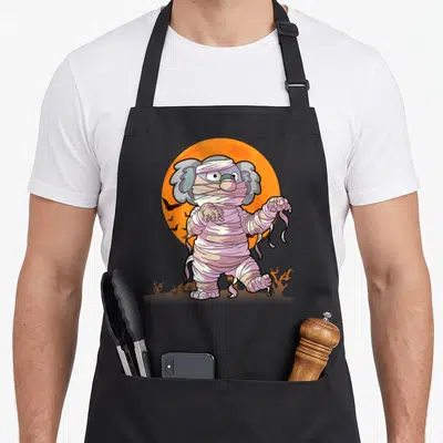 Tablier de cuisine noir avec illustration d'un koala momie aux bandages roses devant une lune orange.