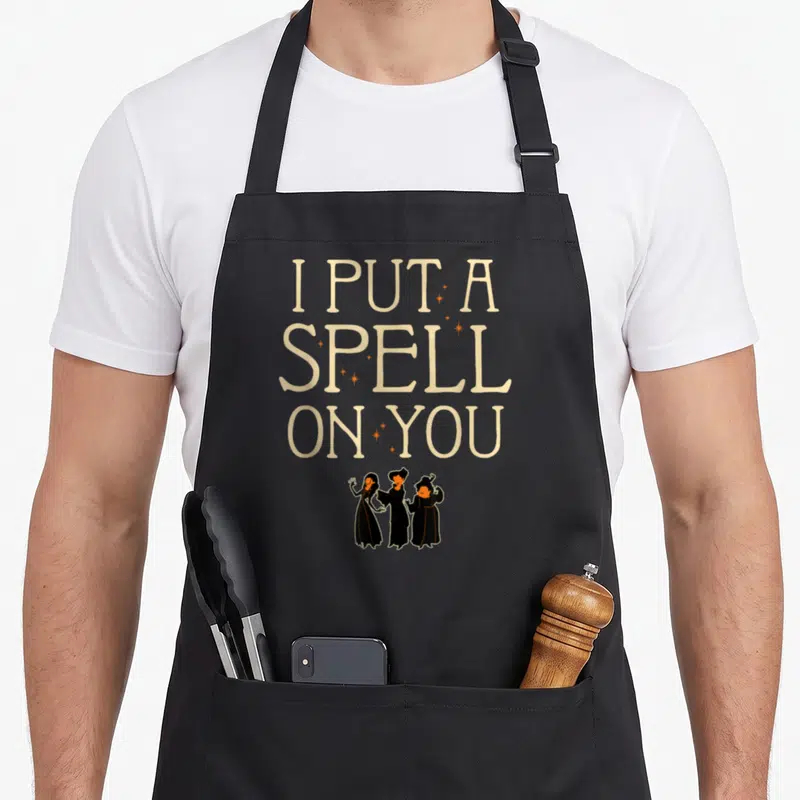 Tablier de cuisine noir avec l'inscription I Put A Spell On You et trois petites sorcières en bas.