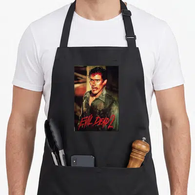 Tablier de cuisine noir avec illustration d'Ash Williams et le texte Evil Dead 2 en rouge.
