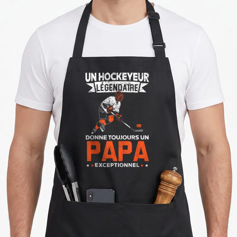 Tablier de cuisine noir avec illustration d'un joueur de hockey et texte blanc et orange sur fond uni.
