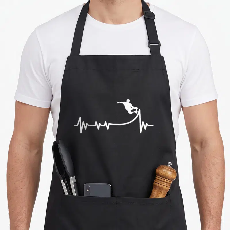 Tablier de cuisine noir avec silhouette blanche de skateur effectuant un saut au-dessus d'une ligne de rythme cardiaque stylisée.
