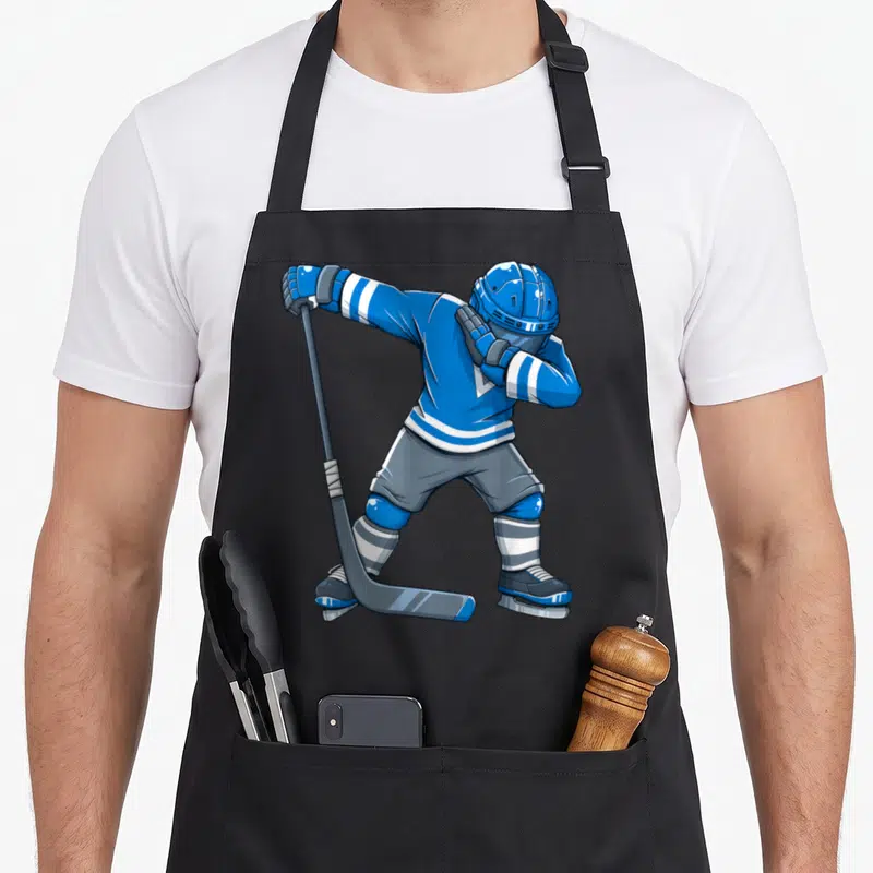 Tablier de cuisine noir avec un joueur de hockey en tenue bleue effectuant un dabber avec son bâton.