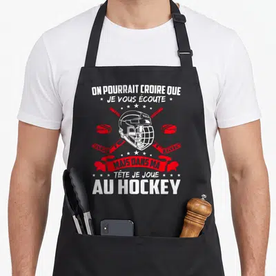 Tablier de cuisine noir avec un casque de hockey blanc, deux sticks rouges croisés et une phrase humoristique en blanc et rouge.