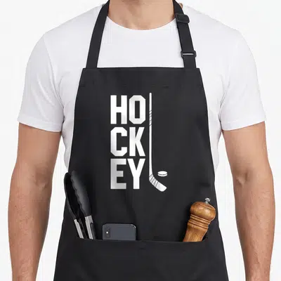 Tablier de cuisine noir avec le mot HOCKEY en blanc et une illustration de crosse et de palet.