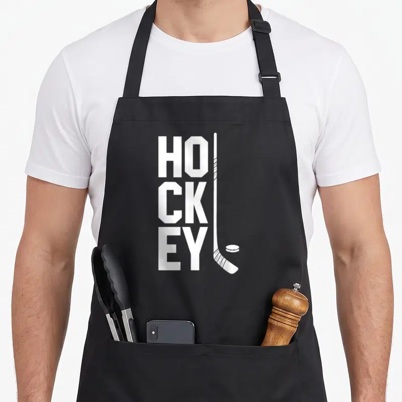 Tablier de cuisine noir avec le mot HOCKEY en blanc et une illustration de crosse et de palet.