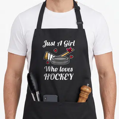 Tablier de cuisine noir avec crosse, palet et texte Just A Girl Who Loves Hockey orné de petits coeurs rouges.
